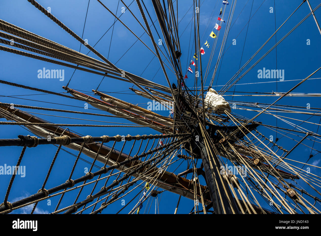 Parte náutica de un yate o un velero grande y antigua con cuerdas, jarcia, velas, mástiles, nudos, banderas de señales delante de un cielo azul Foto de stock