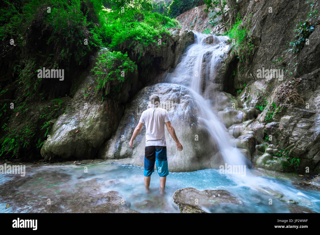 Viajero solitario hombre de pie delante de una cascada en la selva. Foto de stock