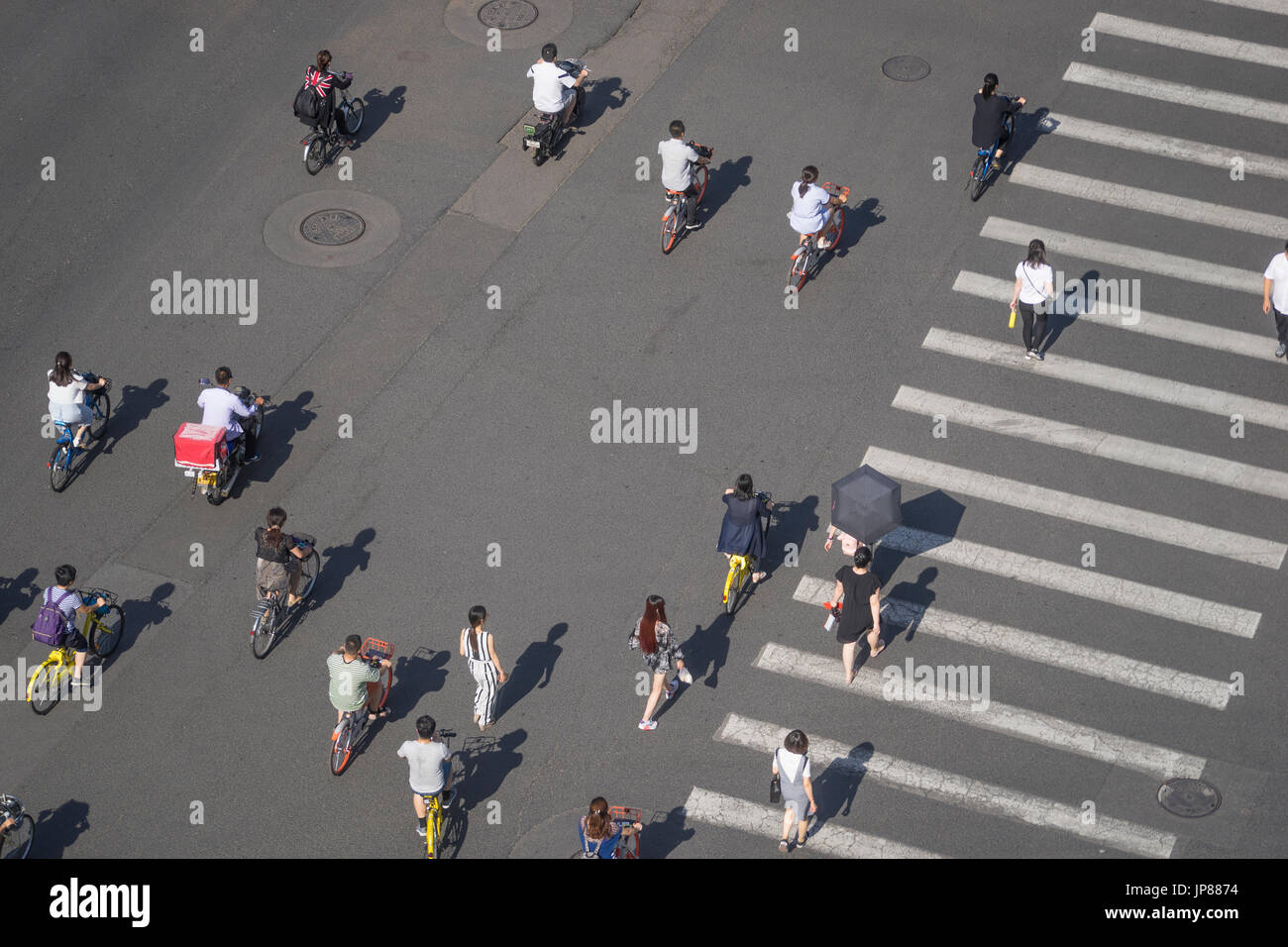 Los peatones, ciclistas y motos cruzando la calle a través de un paso de peatones, mientras que los taxis esperan caminar a través de una amplia calle de la ciudad con paso de peatones Foto de stock