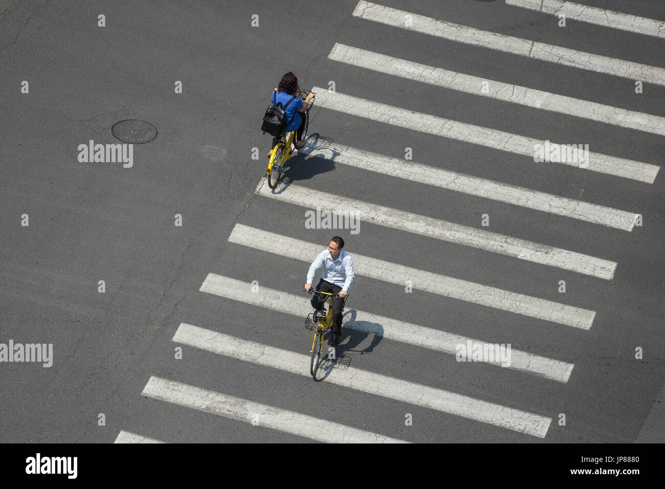Vista aérea de dos personas en bicicleta a través del paso de peatones de una carretera ancha proyecte sombras sobre las líneas Foto de stock