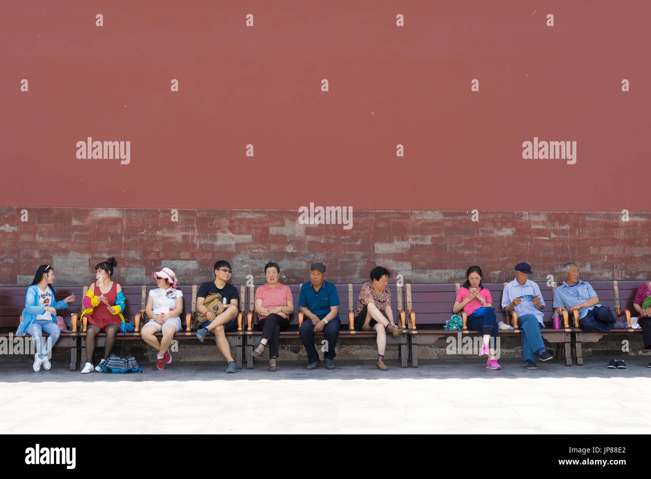 Los turistas chinos de diferentes edades, sentados en un banco en la Ciudad Prohibida en Beijing - algunos descansando, algunos hablando, uno en su teléfono móvil Foto de stock