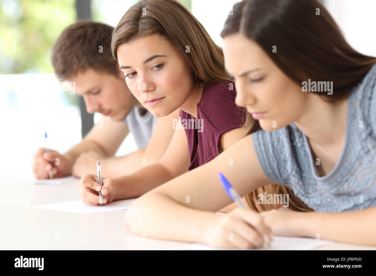 Estudiante intentando copiar un examen de la enojada classmate en un aula. Foto de stock