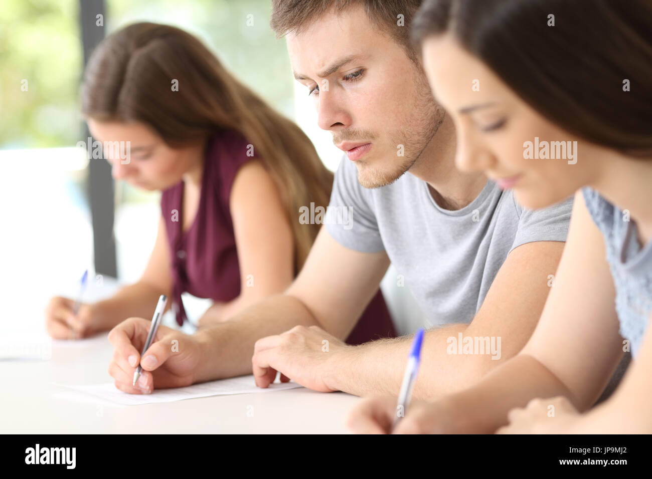 Vista lateral de un estudiante intenta copiar un examen de una compañera de clase en un aula. Foto de stock