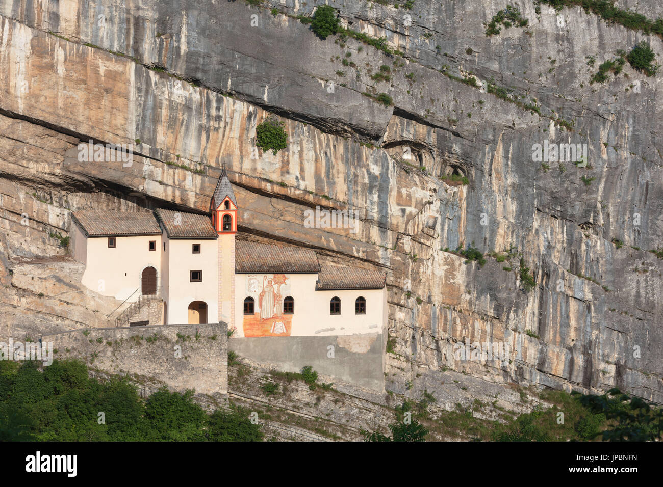 Una vista del Eremo di San Colombano, un monasterio en Trambileno, provincia de Trento, Italia, notable por su ubicación en la ladera de una montaña. Foto de stock