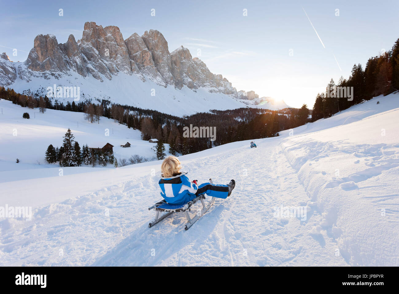 Un niño va abajo con un trineo durante un hermoso atardecer en Villnoss con el Geisler en el fondo, la provincia de Bolzano, Tirol del Sur, Trentino Alto Adige, Italia, Europa Foto de stock