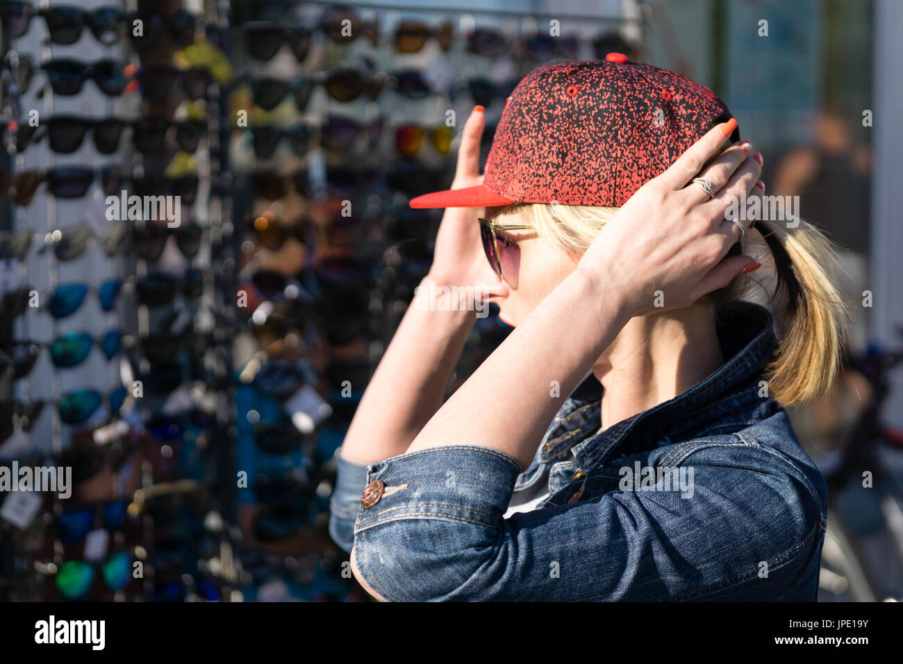 La mujer está tratando de gorra roja al aire libre. Fondo con el mercado con un montón de gafas de sol Foto de stock