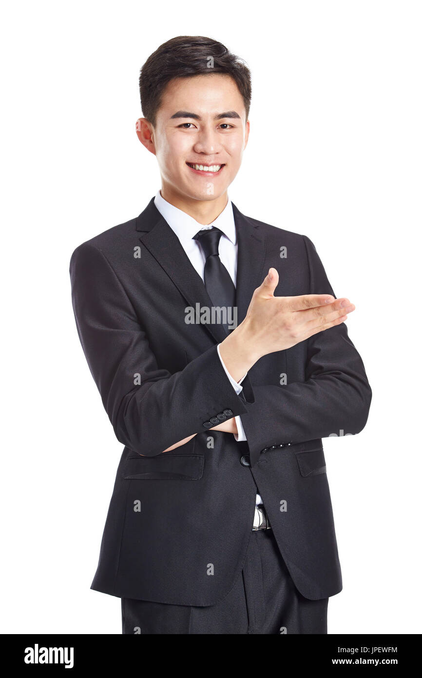 Joven empresario asiático en desgaste formal gesticulando una invitación, feliz y sonriente, aislado en blanco procedencia. Foto de stock