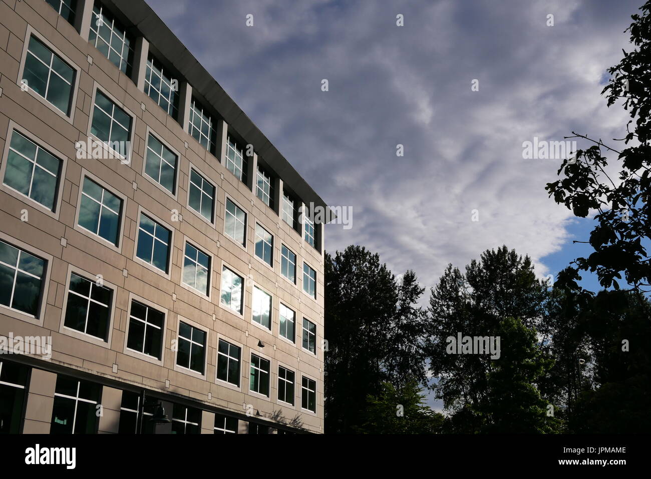 Cielo nublado con fachada de cristal iluminado refleja el moderno edificio de oficinas Foto de stock