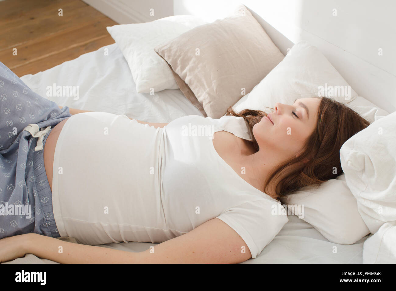 Mujer sonriente embarazada acostada en la cama Foto de stock