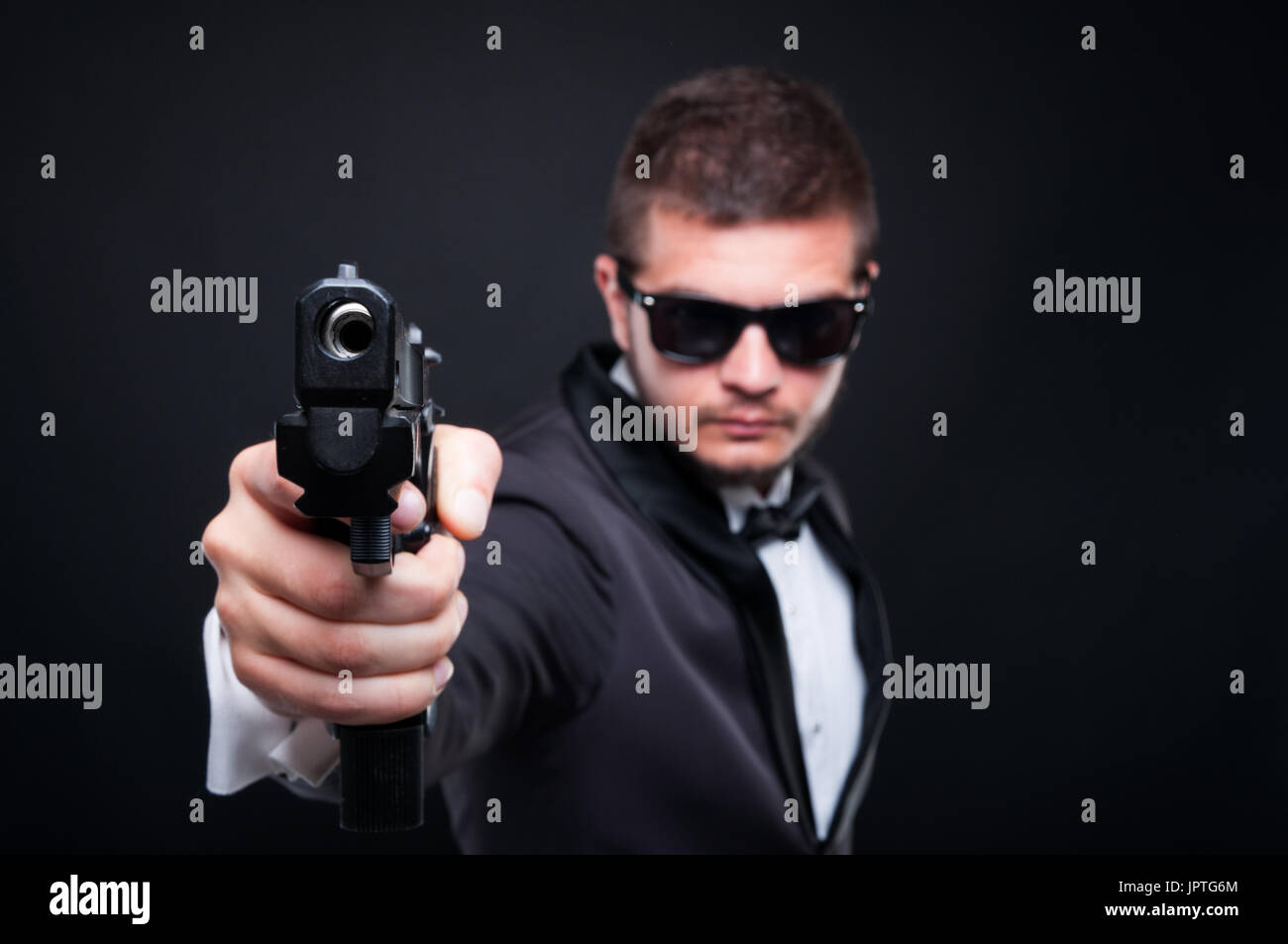 Apuesto asesino pistola apuntando a una meta invisible intentando intimidar sobre fondo oscuro Foto de stock