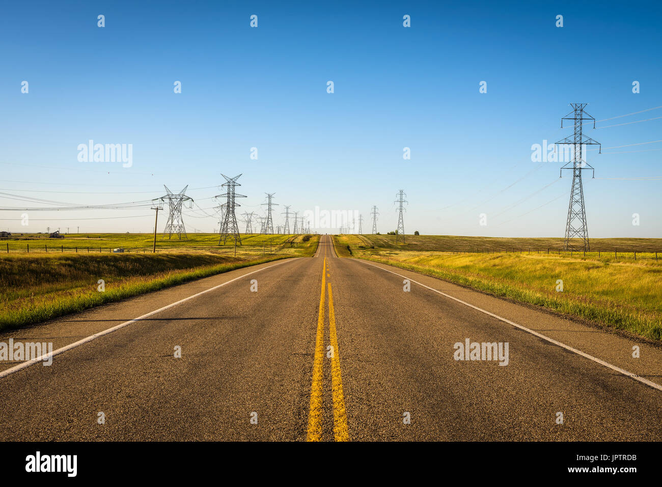 Altos pilares con electricidad , líneas de transmisión a lo largo de una carretera vacía en Alberta, Canadá Foto de stock