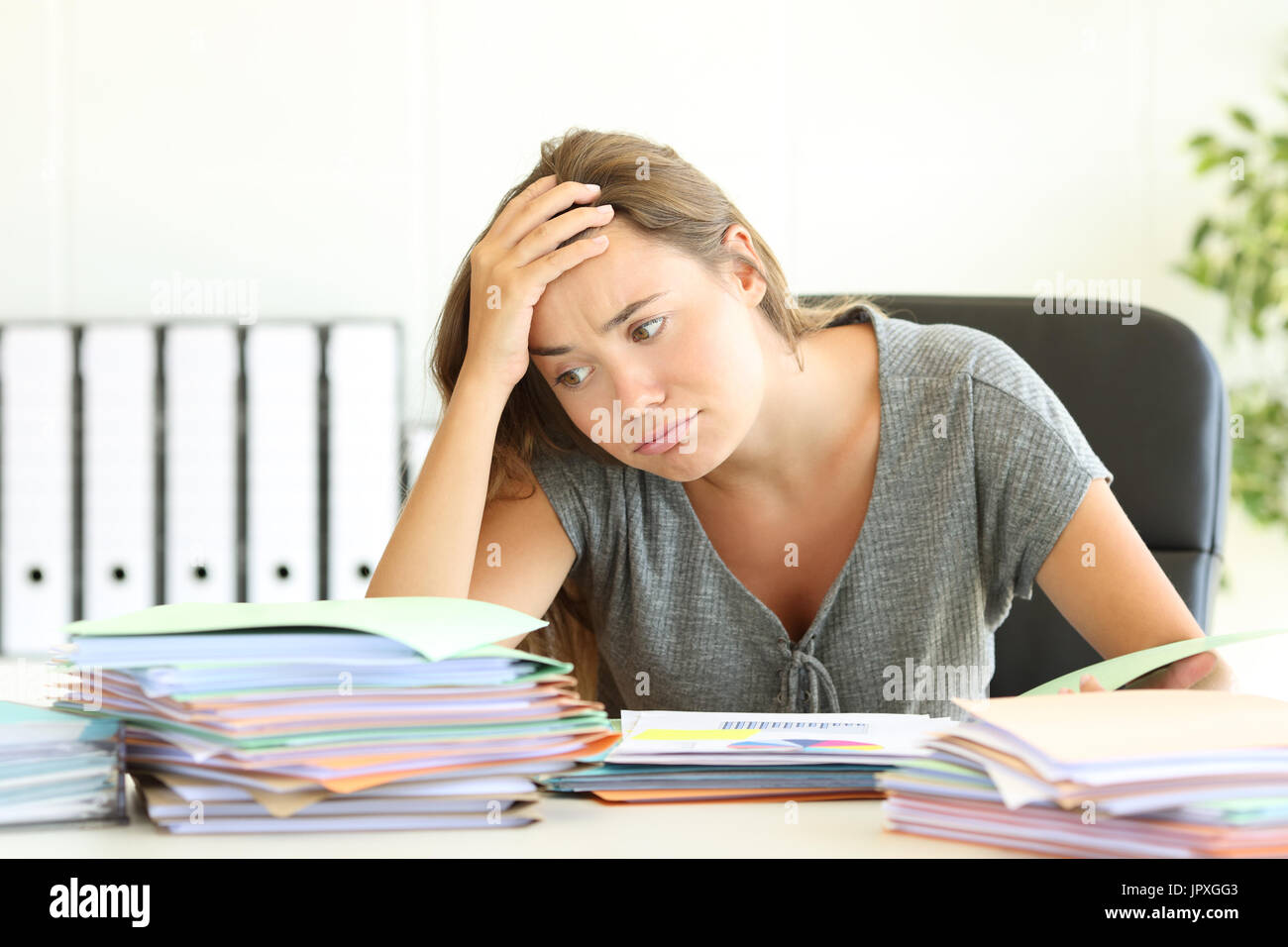 Retrato de un sobrecargado de trabajo empleado cansado mirando un montón de documentos sobre un escritorio en la oficina Foto de stock