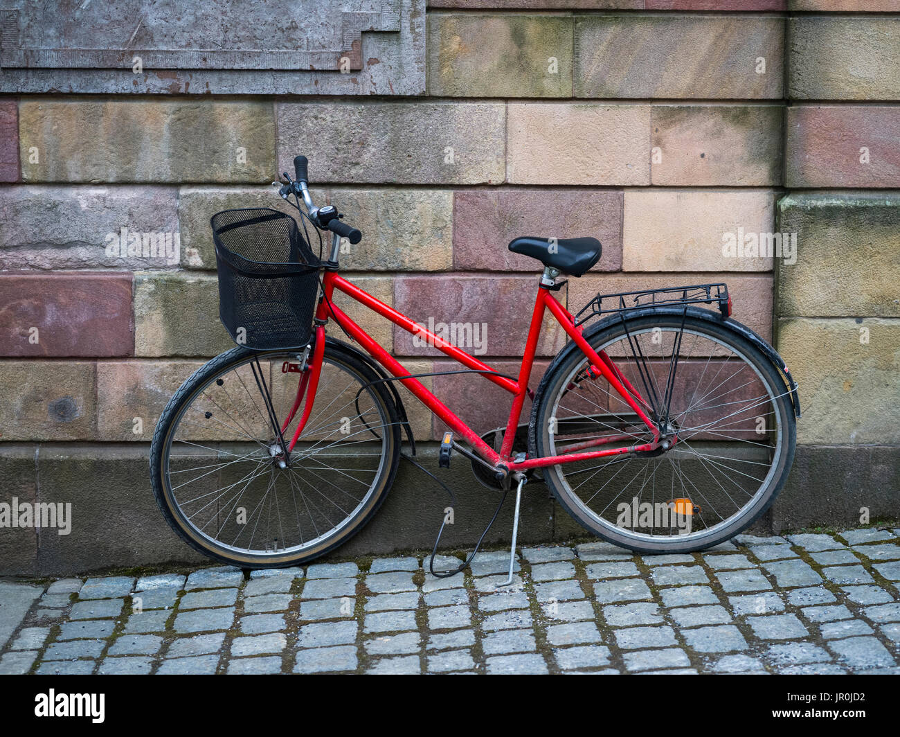 Una bicicleta roja estacionada contra una pared de bloques de piedra; Estocolmo, Suecia Foto de stock