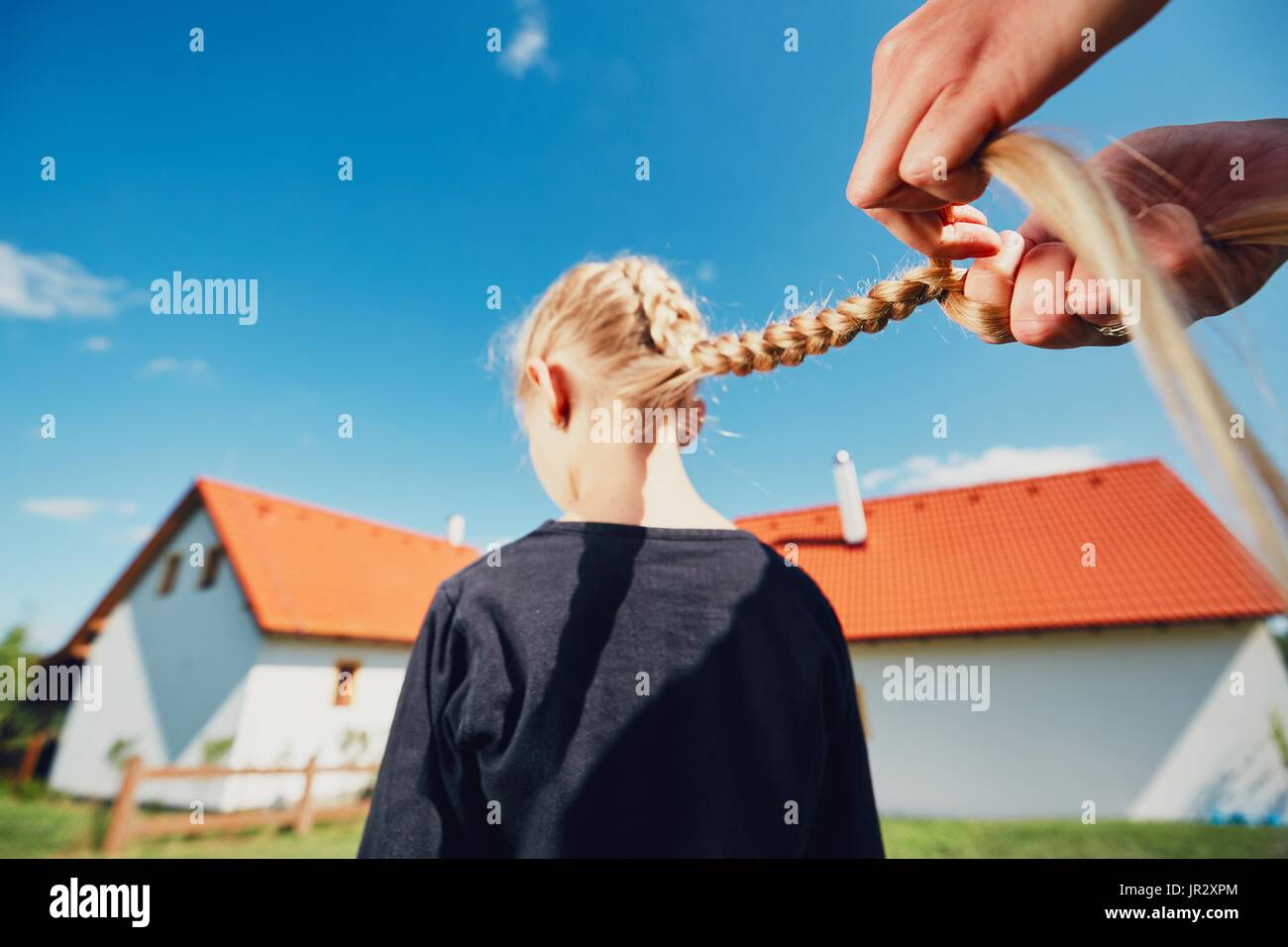Mujer joven haciendo que el cabello trenzas de la niña en el jardín en el paisaje. Foto de stock