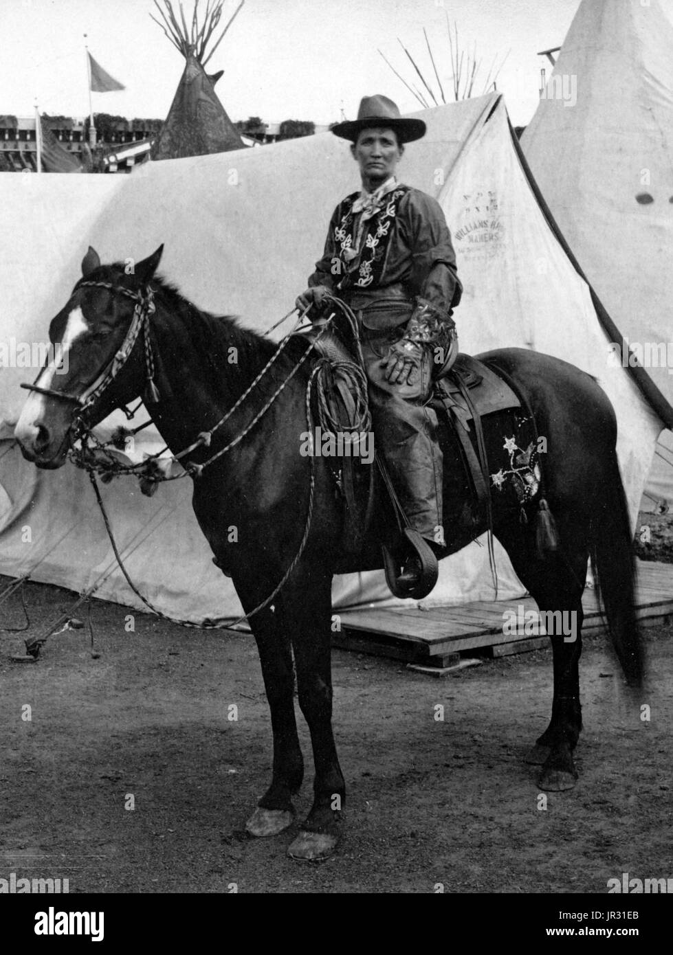 Calamity Jane, a caballo, vistiendo un traje occidental elaborada, delante de tipis y tiendas de campaña en la Exposición Panamericana en Buffalo, Nueva York, 1901. Martha Jane Canary (1 de mayo de 1852 - 1 de agosto de 1903), mejor conocido como Calamity Jane, fue un norteamericano frontierswoman scout y profesional. Ella recibió poca o ninguna educación formal y era analfabeta. Trabajó como un lavaplatos, un cocinero, una camarera, un salón de baile chica, una enfermera y un buey team. En 1874, encontró trabajo como scout en Fort Russell. En 1876 se radicó en la zona de Deadwood e hizo amistad con Wild Bill Hickok y Char Foto de stock