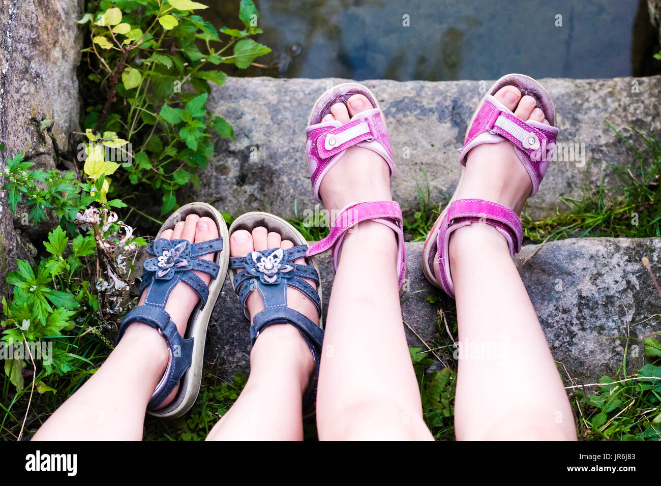 Las piernas de la muchacha con sandalias. Pie en sandalia roja sobre la  piedra de las escaleras. La hierba verde Fotografía de stock - Alamy