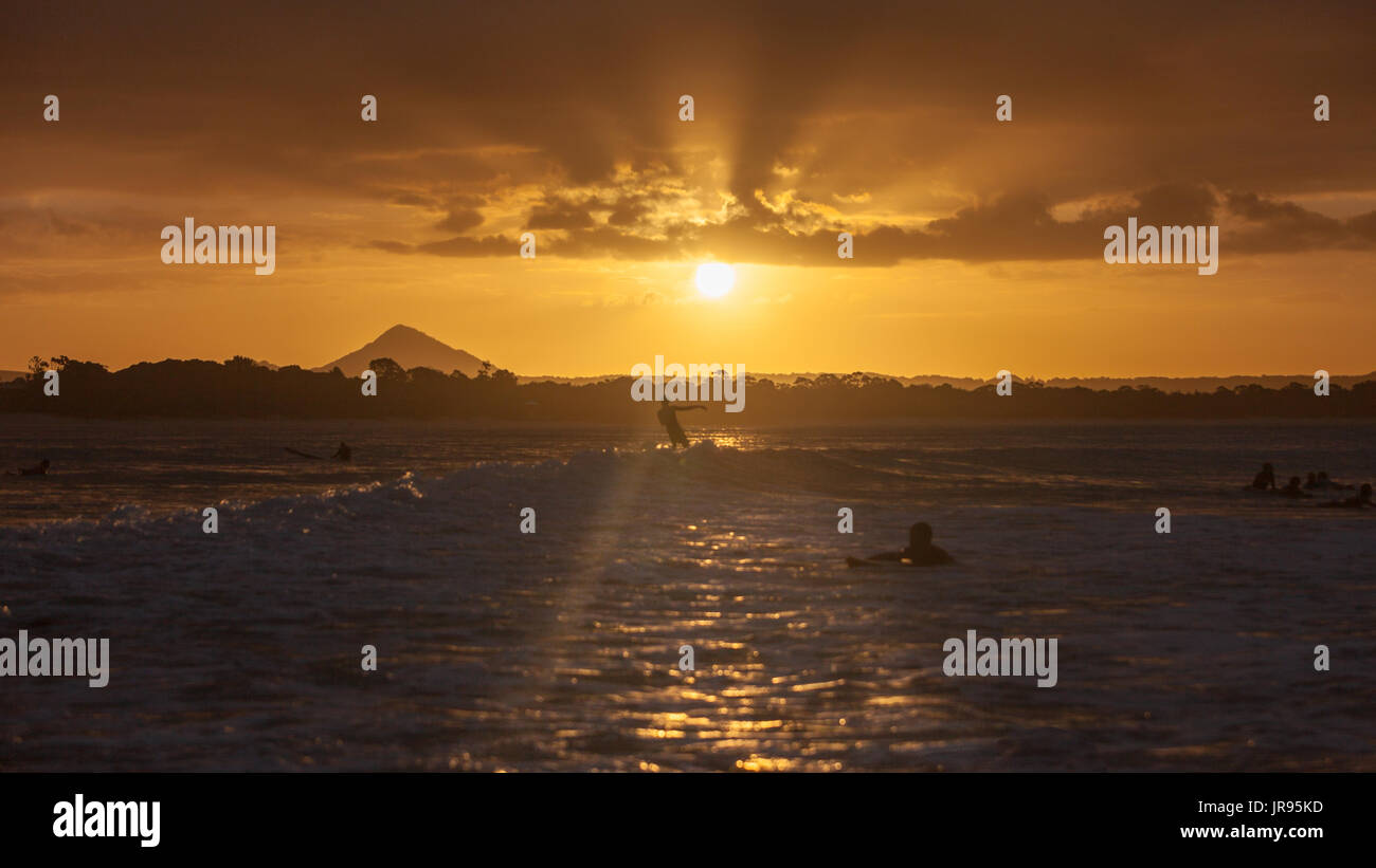 Sunset encima de Noosa Heads, Queensland con un surfista cabalgando una ola, fotografiado por detrás. Foto de stock