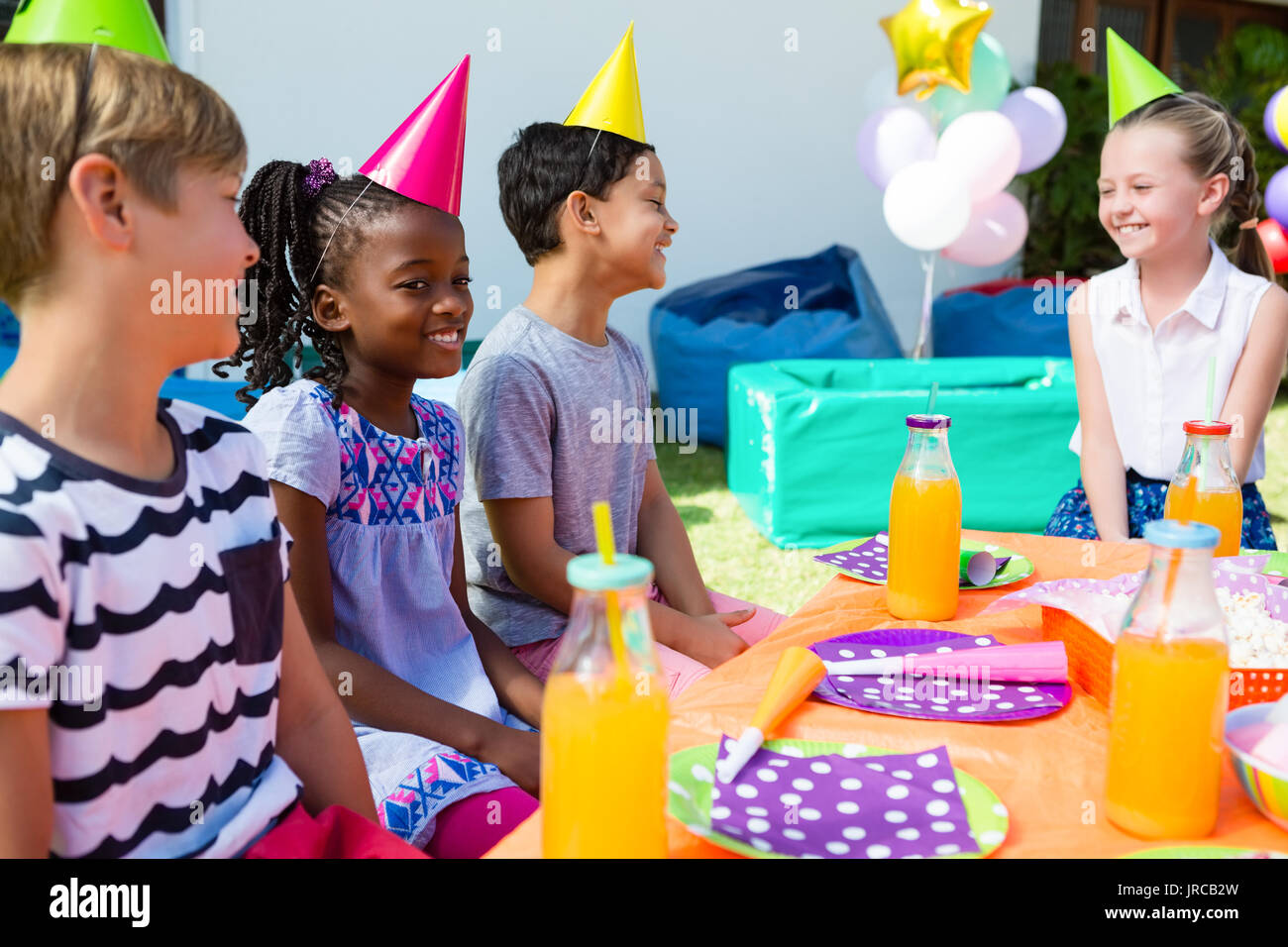 Los niños felices de hablar mientras se está sentado en la mesa durante la fiesta de cumpleaños Foto de stock