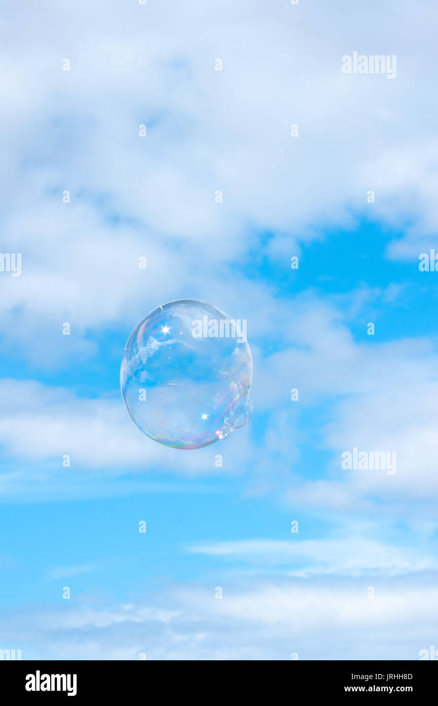 Burbuja grande flotando en un claro cielo de verano azul con nubes blancas mullidas. Foto de stock
