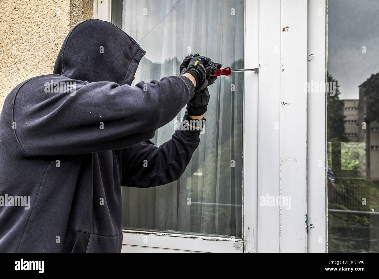 Imagen de símbolo, Apartamento el robo, el ladrón intenta irrumpir en un apartamento, rompiendo una ventana con la herramienta, Foto de stock