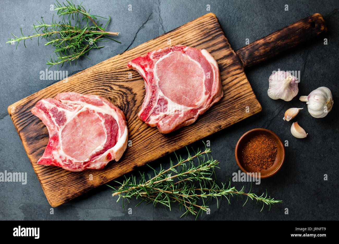 Chuleta de cerdo crudo pique para freír en la sartén con hierbas, ajo sobre  tablas de madera, fondo gris pizarra Fotografía de stock - Alamy