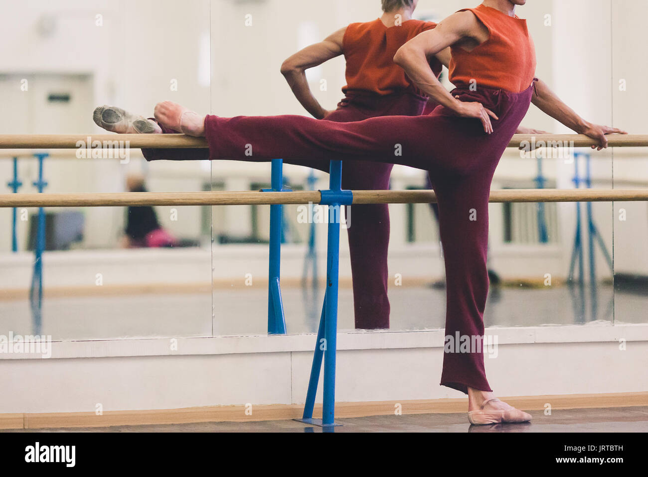 La danza, el de belleza. Dura bailarina de ballet vistiendo pantalones de chándal acogedor en granate y zanahoria-rojo sin mangas haciendo ejercicios en la sala de baile coreográfico