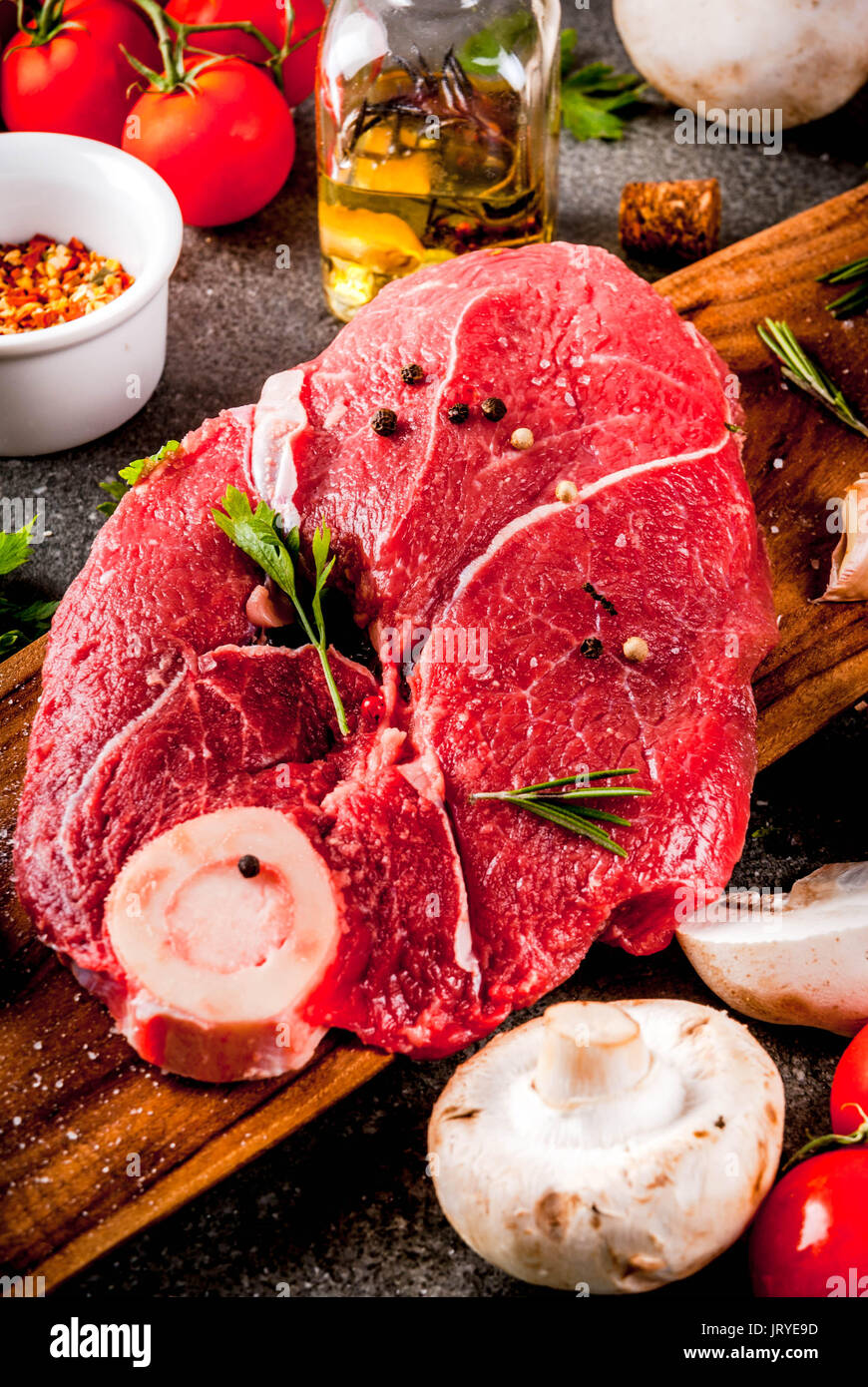 La carne cruda con los ingredientes para la cena. Filete de ternera, lomo, sobre la placa de corte, con sal, pimienta, perejil, romero, aceite, ajo, tomate, champiñones, Foto de stock
