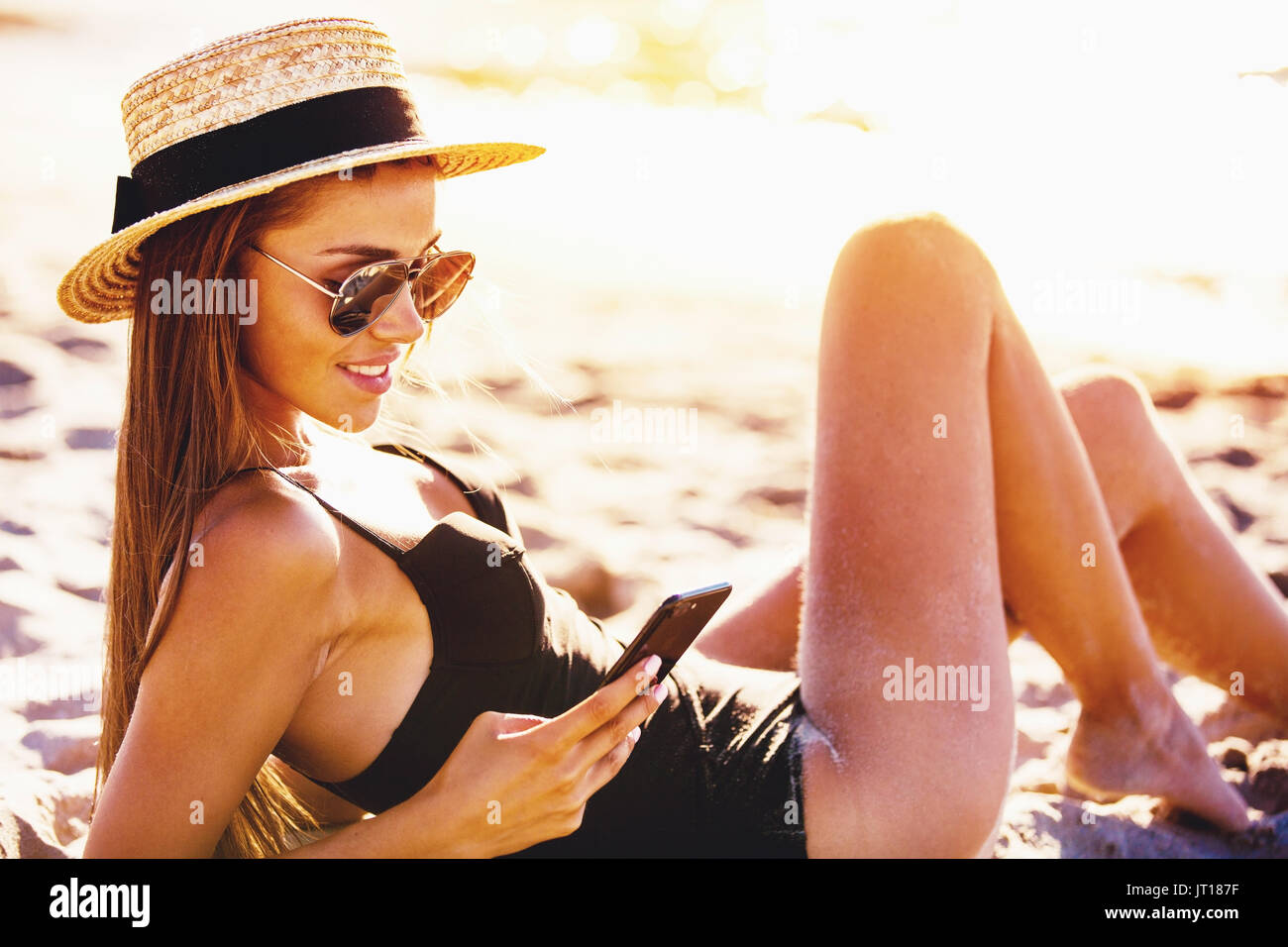 Hermosa chica envía un mensaje con su smartphone en la playa. Foto de stock