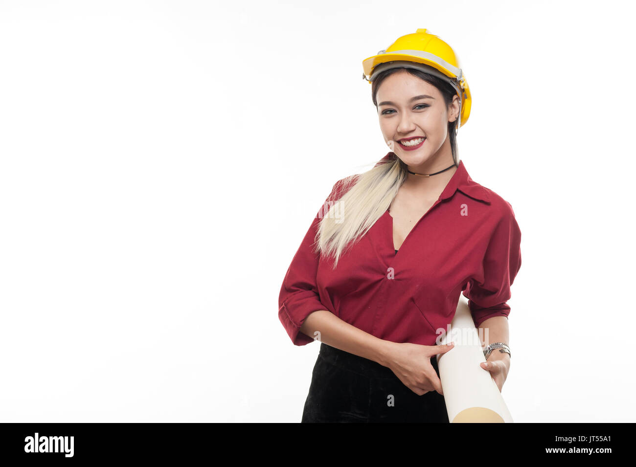 Joven mujer asiática arquitecto con camiseta roja y casco de seguridad amarillo sonriendo mientras transportaba blueprint papeles. La ocupación industrial las personas concepto Foto de stock