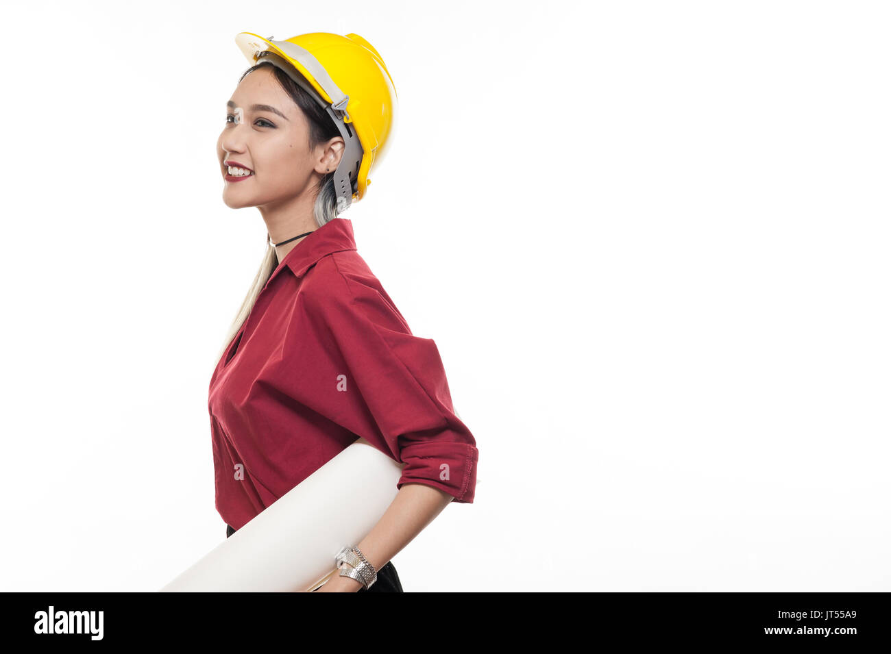 Joven mujer asiática arquitecto con camiseta roja y casco de seguridad amarillo sonriendo mientras transportaba blueprint papeles. La ocupación industrial las personas concepto Foto de stock