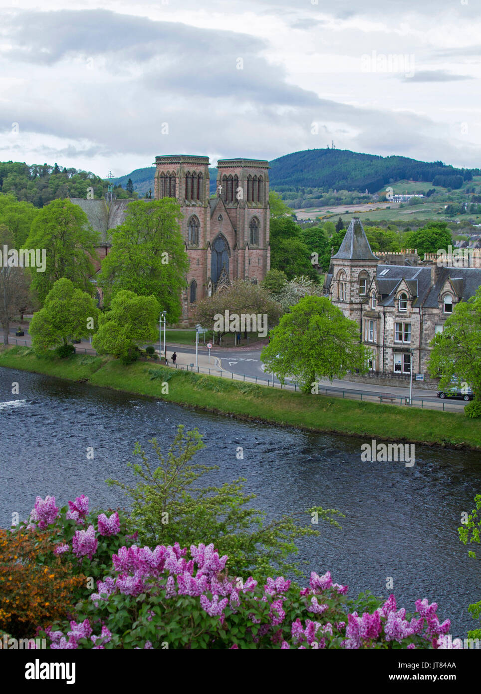Ciudad de Inverness con edificios históricos, árboles y flores bordeando el río Ness, con montañas en el fondo en Escocia Foto de stock