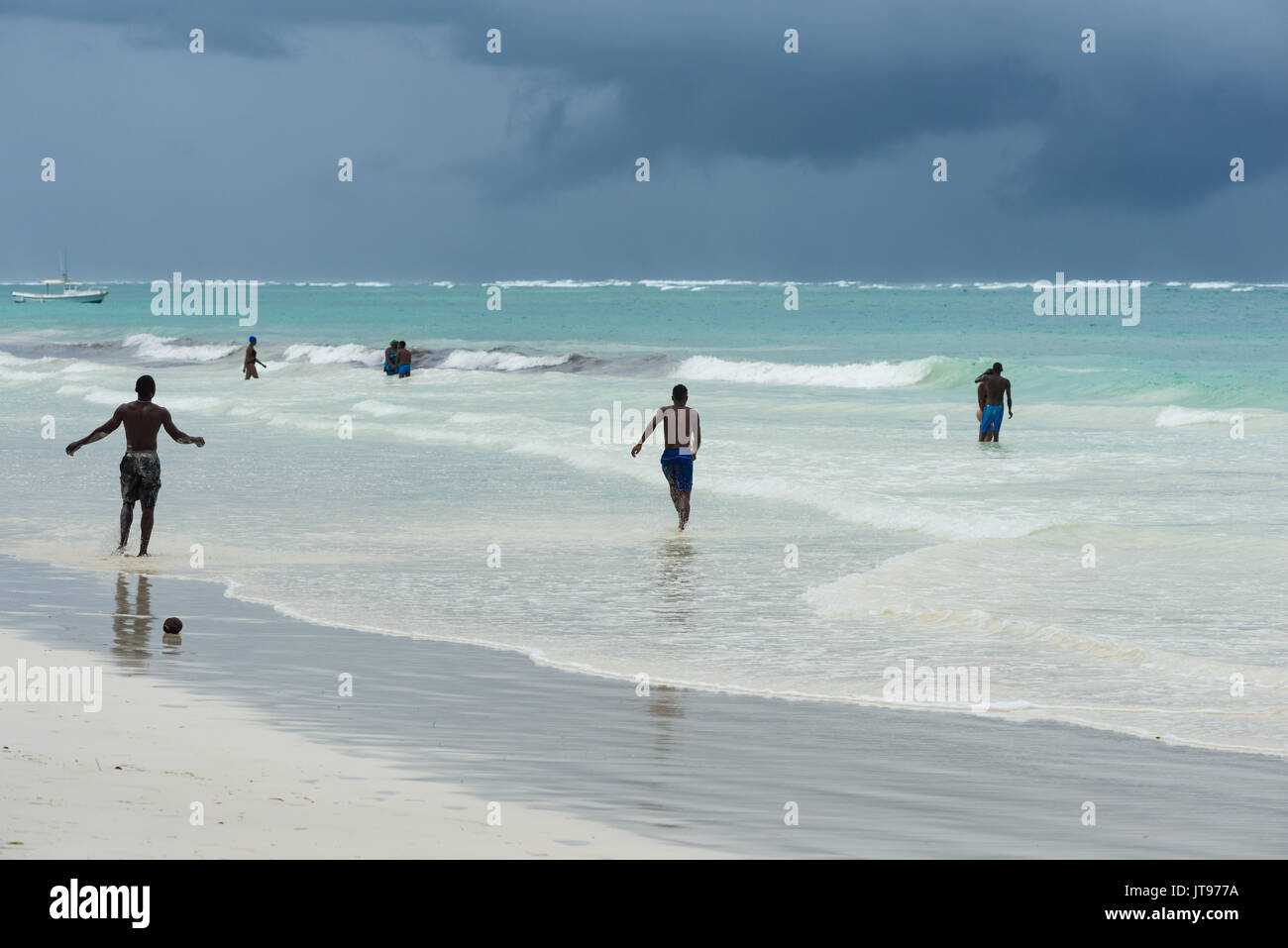 Personas jugando en el océano por la playa con nube de lluvia en el fondo, Diani, Kenya Foto de stock