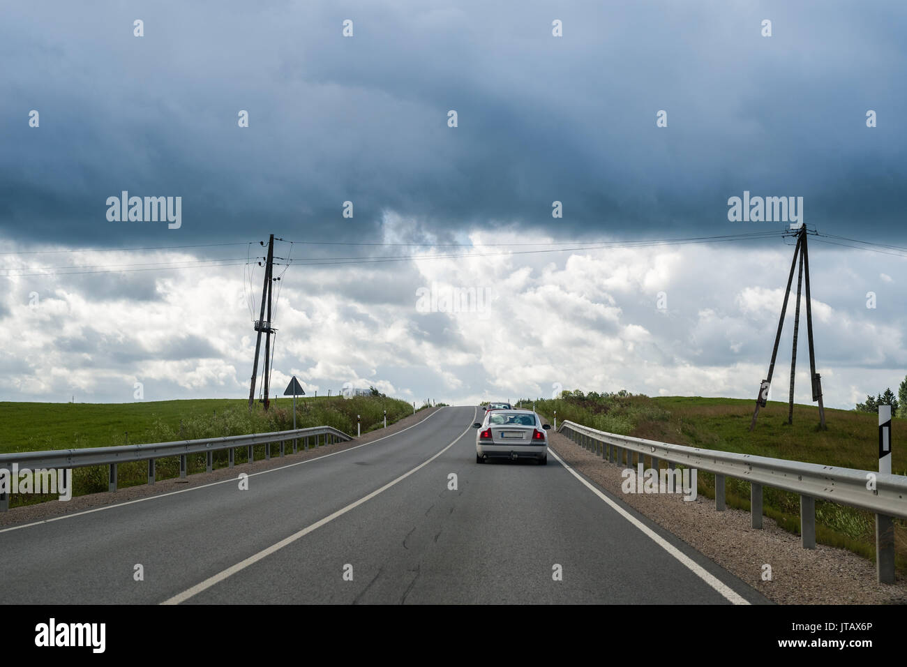 Coche subiendo la colina en Country Road en nublado día de verano en Letonia Foto de stock