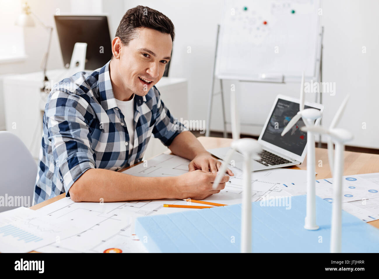 Los ajustes necesarios. Encantador joven arquitecto sentado en la mesa y hacer algunos cambios en su plan de acuerdo a las particularidades del viento t Foto de stock