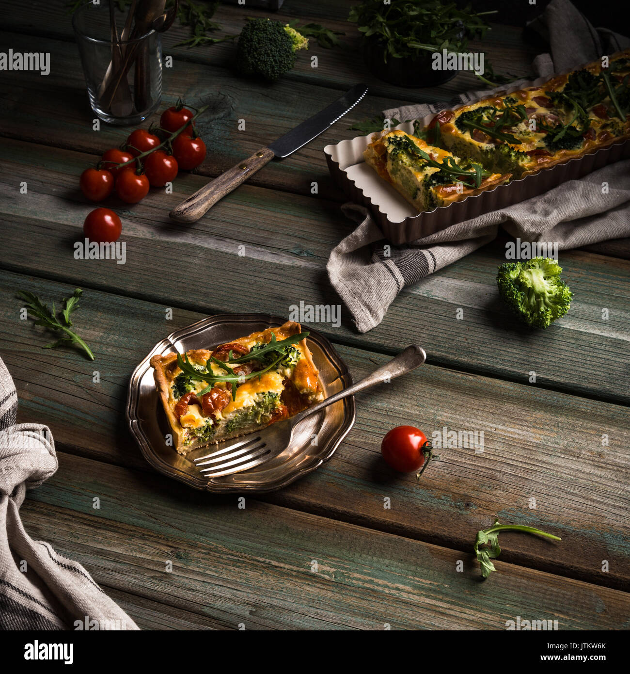 Rodaja de deliciosa quiche casera con tomates cherry y brócoli sobre placa de metal. Foto oscura de sana comida vegetariana. Foto de stock
