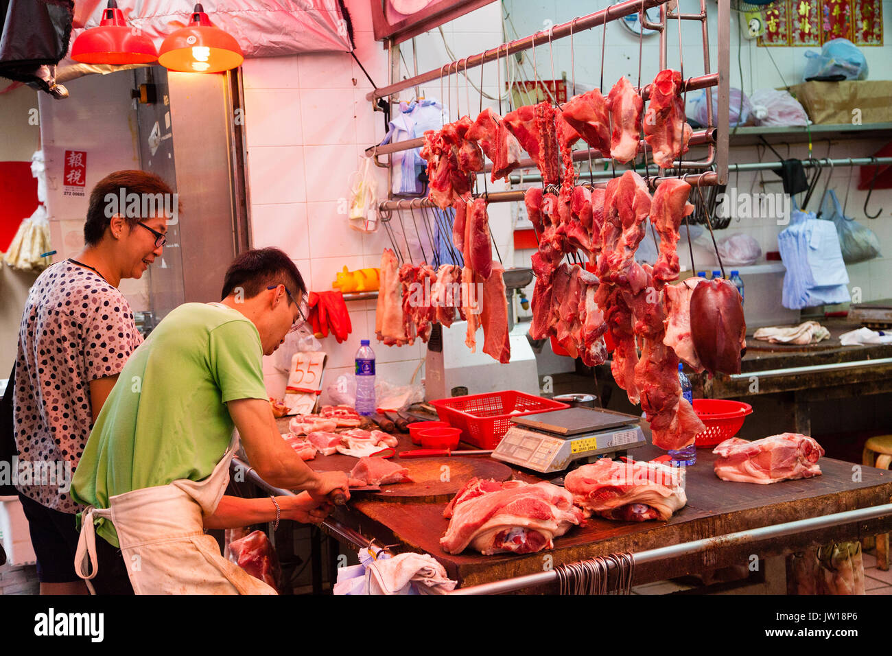 HONG KONG - Julio 7, 2017: un carnicero cortar un trozo de carne de cerdo para un cliente en un mercado callejero Shui Po Shum en Hong Kong. Foto de stock
