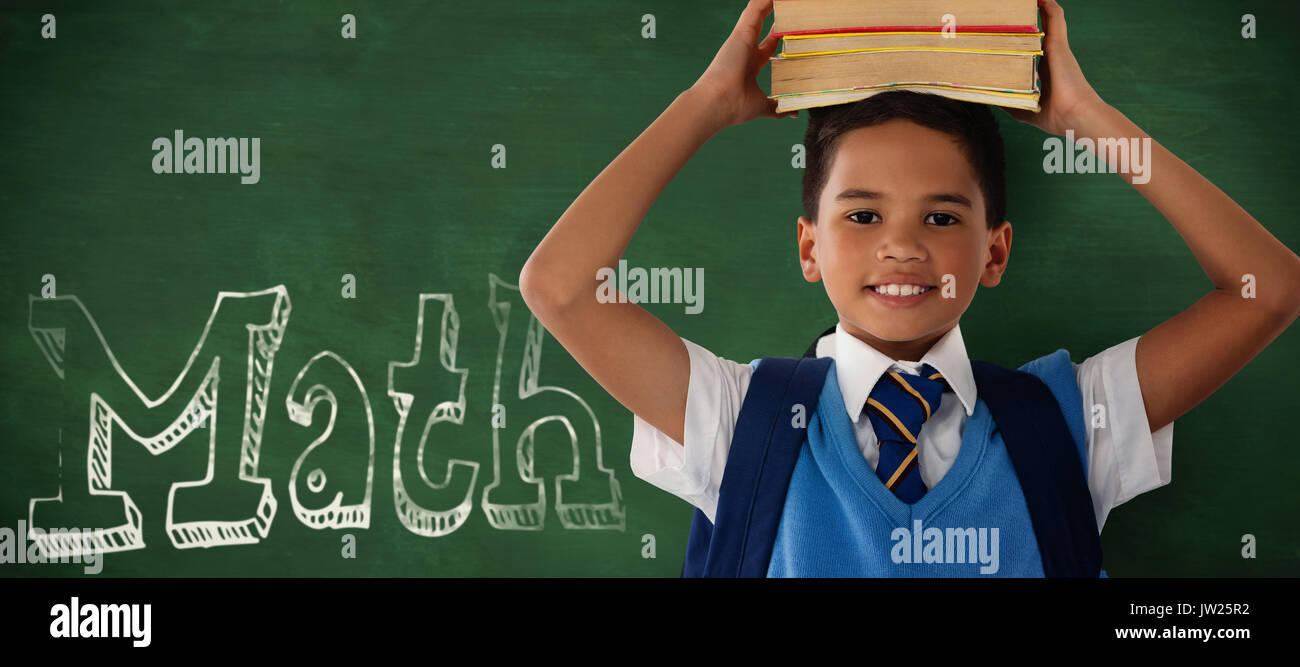 Sonriendo colegial llevar libros en la cabeza sobre fondo blanco contra el fondo verde Foto de stock
