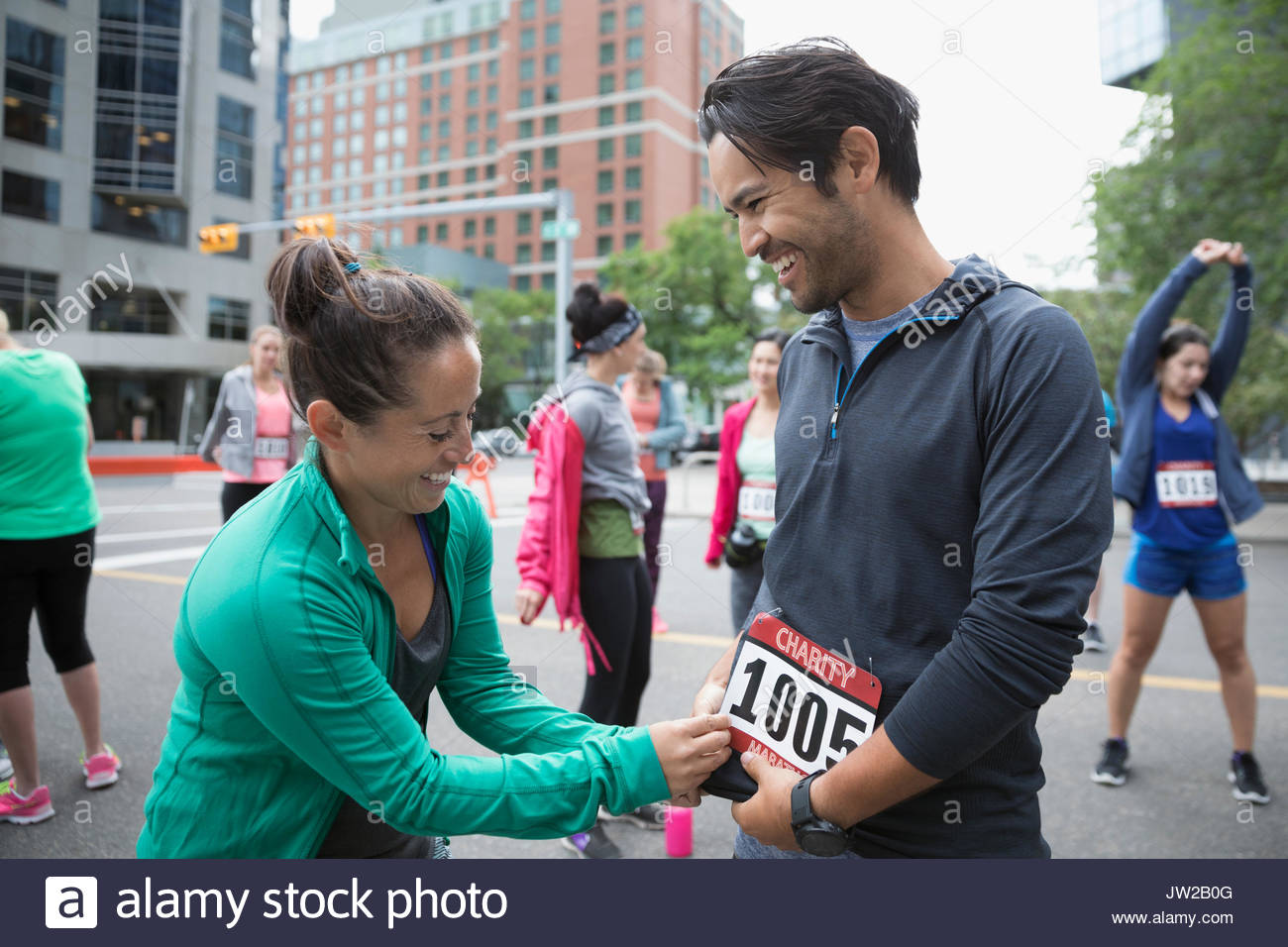 Esposa ayudando sonriente marido puso en maratón bib en la calle urbana Foto de stock