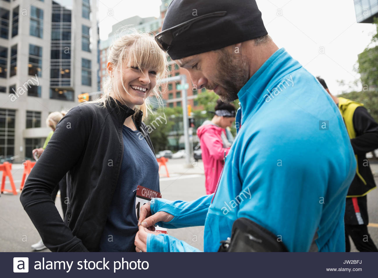 Marido ayudando sonriente esposa puso en maratón bib en la calle urbana Foto de stock