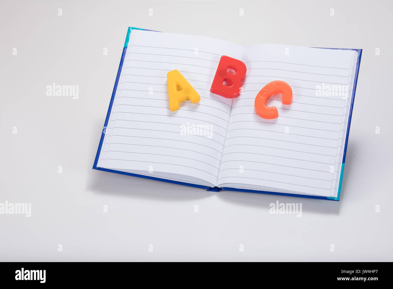 Abrir un libro escolar en blanco, con el aprendizaje de las letras del alfabeto ABC multicolores y llano fondo blanco con espacio de copia. Foto de stock