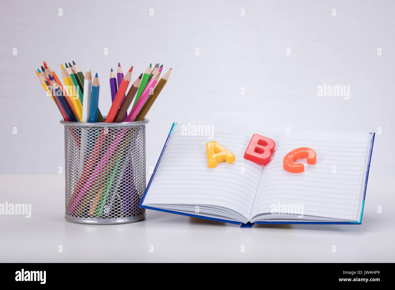 Un concepto de aprendizaje escolar con color lápices para dibujar un libro abierto y el aprendizaje de las letras del alfabeto ABC sobre un fondo completamente blanco con espacio de copia. Foto de stock