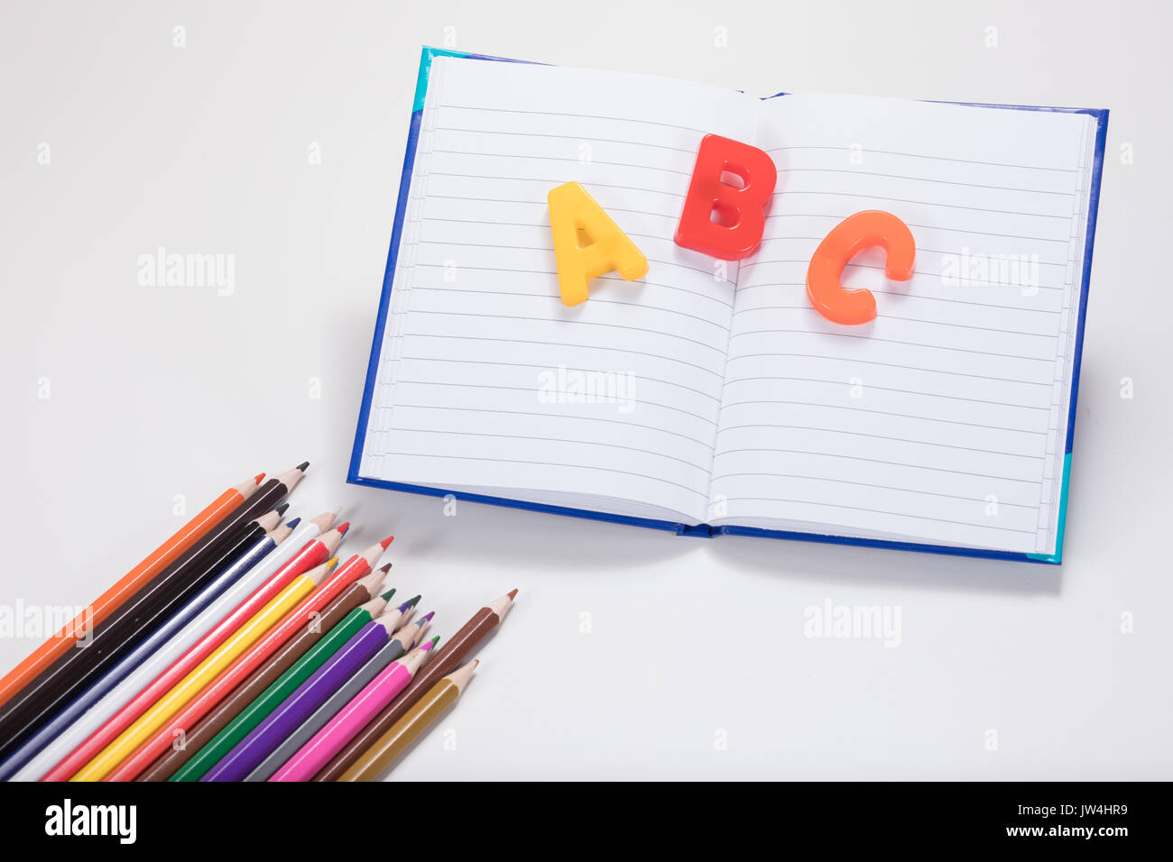 Un concepto de aprendizaje escolar con lápices de colores, libros de escuela abierta y ABC de las letras del alfabeto en una llanura fondo blanco con espacio de copia. Foto de stock
