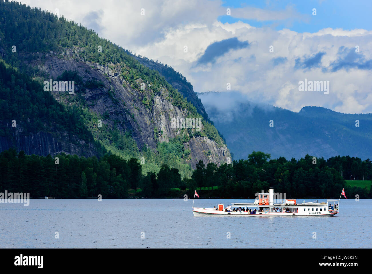 Bygland, Noruega - Agosto 1, 2017: Viaje documental de turistas montando el museo de barcos de vapor Bjoren en lago de montaña. Paisaje oscuro con la montaña Foto de stock