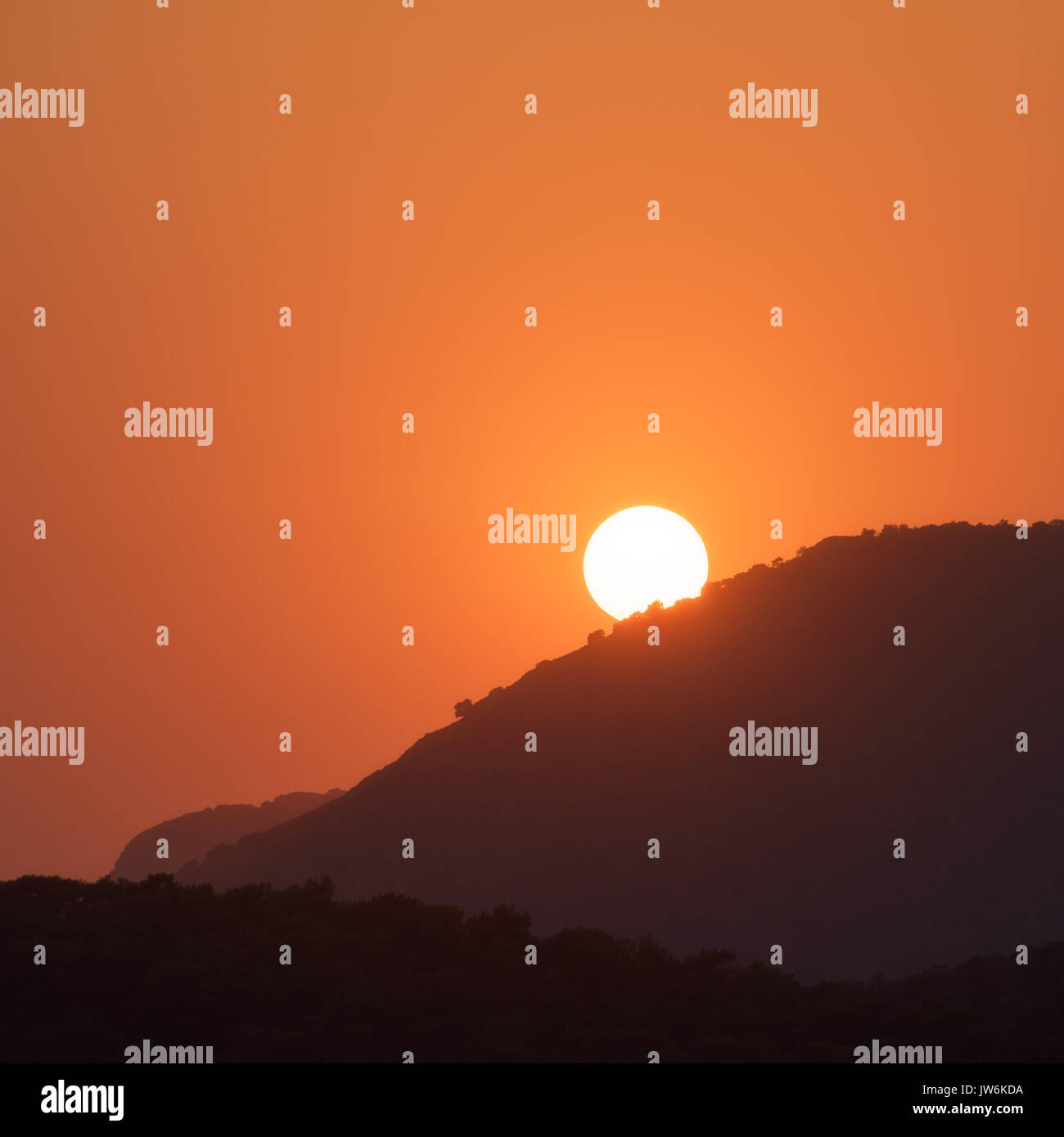 Paisaje minimalista con siluetas de las crestas de las montañas y cielo naranja con sol en verano en el luminoso atardecer.increíbles vistas de las colinas y el disco solar Foto de stock