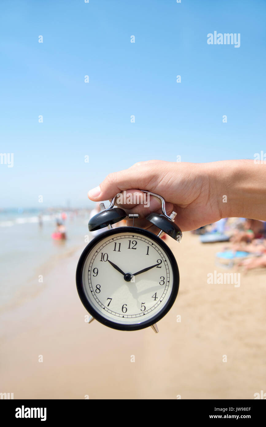 Primer plano de un joven hombre caucásico con un reloj de alarma en su mano en la playa, junto a la orilla del mar, con un espacio vacío en la parte superior Foto de stock