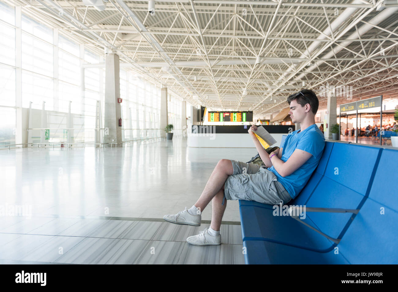 Joven esperando en la sala de embarque de un aeropuerto leyendo un libro Foto de stock