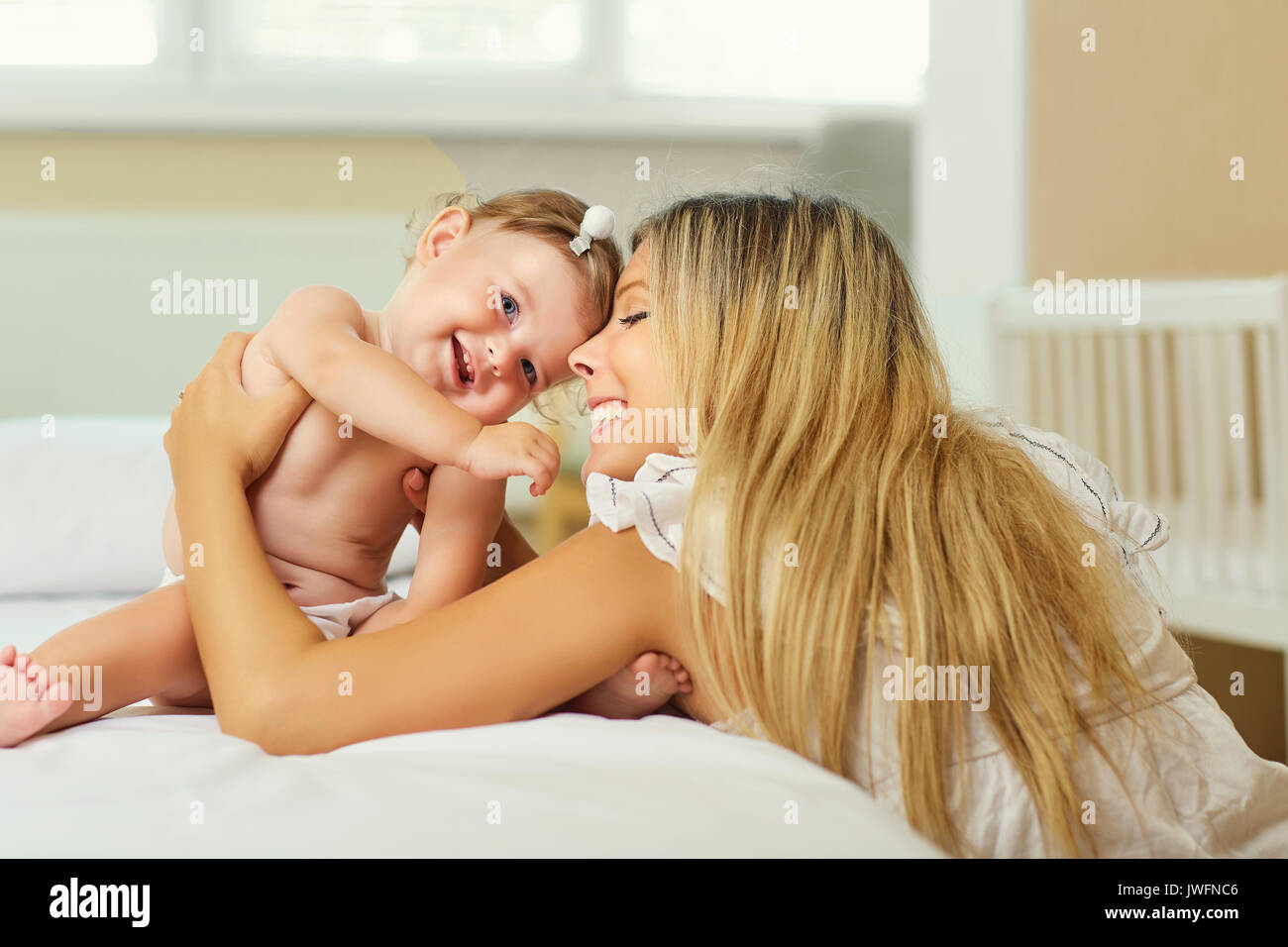 La madre y el bebé en un pañal jugar abrazando en una cama en el interior. Foto de stock