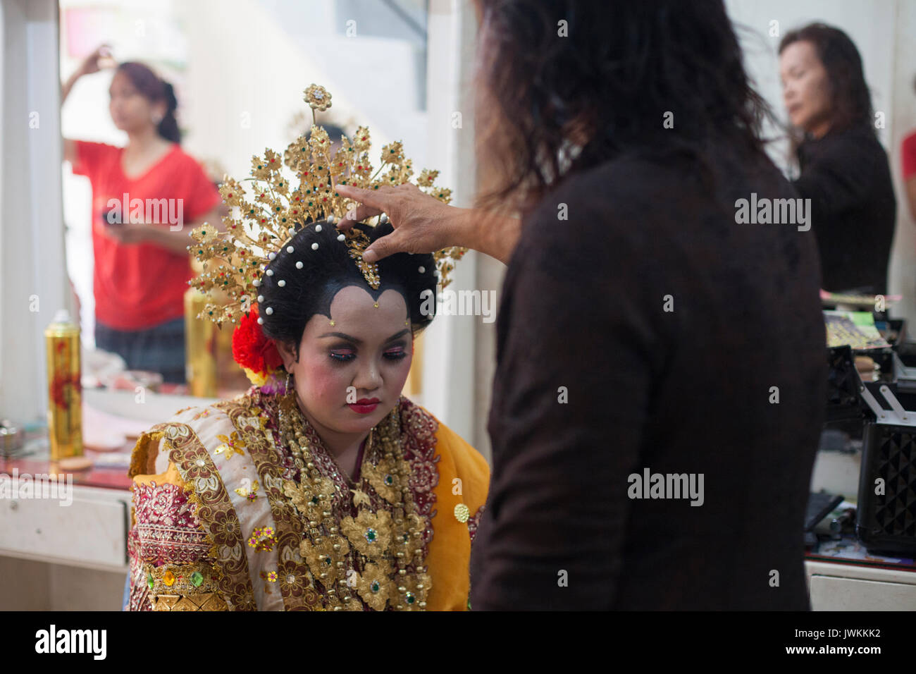 Después de terminar el maquillaje y vestirse Rika, la futura novia, con su vestido de novia, Ibu Haji Hasna le da una bendición final, colocando una mano sobre su cabeza y susurrando una oración. Foto de stock