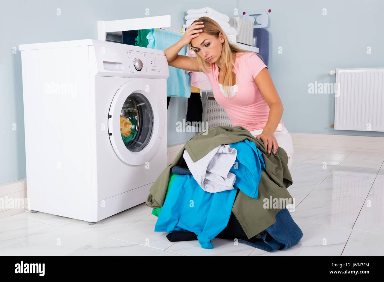 Mujer desgraciada mostrando signos de fatiga, mirando al montón de ropa  cerca de lavadora Fotografía de stock - Alamy