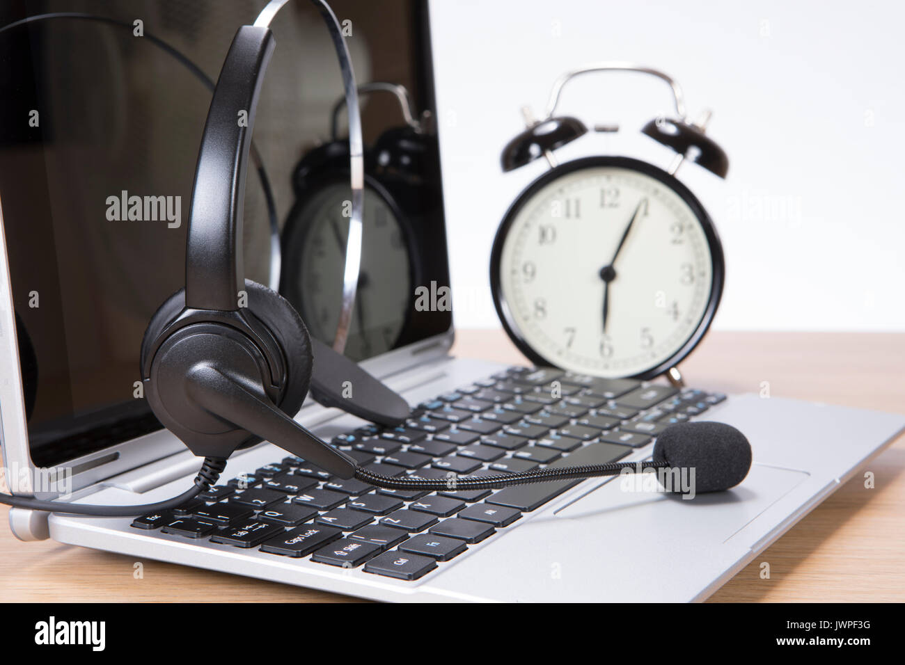 Reloj con alarma y auriculares abiertos en un ordenador portátil con  pantalla en blanco de pie sobre un escritorio de madera n un concepto de  gestión del tiempo, los plazos y las